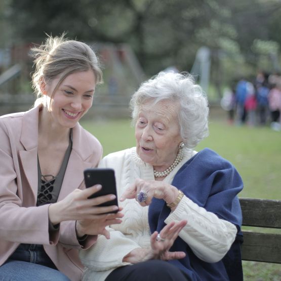 Angehörige und ihre Großmutter sehen sich auf einer Parkbank das Online-Gedenkportal auf dem Smartphone an